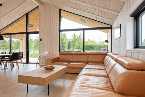 Salon moderne dans une maison de vacances à Sæby, Danemark, avec canapé en cuir et grandes baies vitrées.