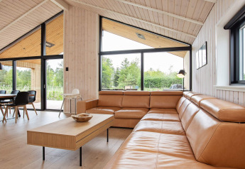 Salon moderne dans une maison de vacances à Sæby, Danemark, avec canapé en cuir et grandes baies vitrées.