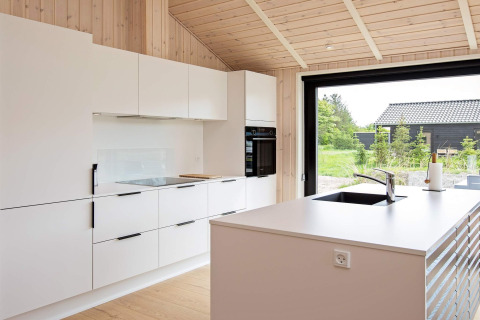 Moderne Küche in einem Ferienhaus in Sæby, Dänemark, mit weißen Schränken und großen Fenstern.