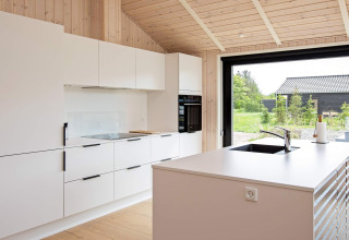 Moderne Küche in einem Ferienhaus in Sæby, Dänemark, mit weißen Schränken und großen Fenstern.