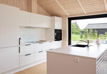 Cocina moderna en casa vacacional para 10 personas en Sæby, Dinamarca, con gabinetes blancos y madera.