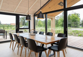 Moderne spisestue i feriehus i Sæby, Danmark, med træbord, sorte stole og store panoramavinduer.