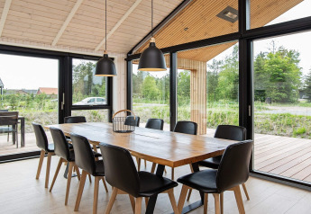 Moderne eetruimte in vakantiehuis in Sæby, Denemarken, met houten tafel en grote ramen.