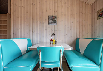 Retro eethoek met turquoise en witte banken, houten wandpanelen en vintage posters in Sæby, Denemarken.