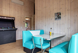 Coin repas rétro avec sièges turquoise, borne d’arcade et murs en bois dans une maison à Sæby, Danemark.