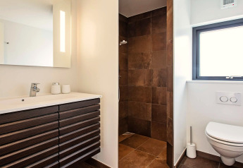 Salle de bains moderne dans une maison de vacances à Sæby, Danemark, avec douche, WC mural et grand miroir.