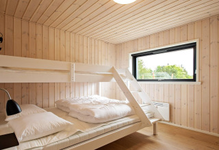 Dormitorio luminoso con litera, paredes de madera y gran ventana en casa de vacaciones en Sæby, Dinamarca.
