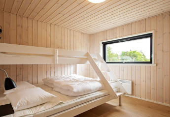 Lichte slaapkamer met stapelbed, houten wanden en groot raam in vakantiehuis in Sæby, Denemarken.