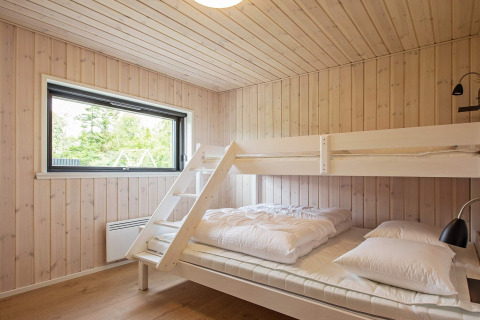Slaapkamer met tweepersoonsbed en stapelbed, lichte houten wanden en raam in vakantiehuis in Sæby, Denemarken.
