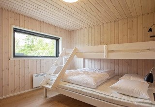 Dormitorio con cama doble y litera, paredes de paneles de madera clara y ventana en casa de vacaciones en Sæby.