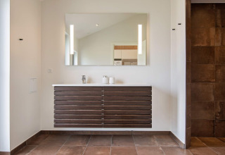 Moderne badkamer met grote spiegel, hangend houten meubel en bruine tegels in vakantiehuis in Sæby.