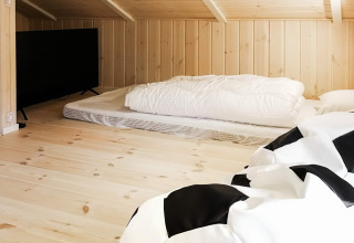 Coin couchage avec matelas et TV sous combles en bois dans maison de vacances à Sæby, Danemark.
