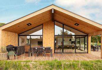 Lodge de vacances moderne en bois à Sæby, Danemark, grande terrasse, salle à manger extérieure et vastes fenêtres.