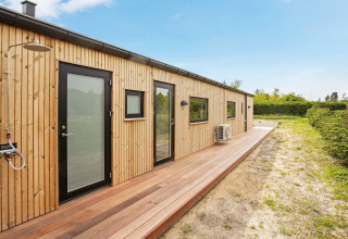 Vista exterior de una casa de vacaciones moderna de madera en Sæby, Dinamarca, con terraza y ducha exterior.
