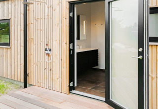 Doccia esterna e porta del bagno aperta in casa vacanze a Sæby, Danimarca, con rivestimento in legno.