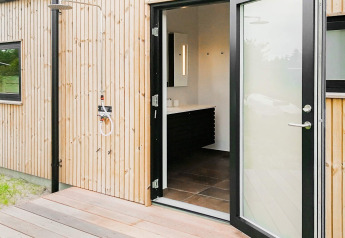 Buitendouche en open badkamerdeur bij vakantiehuis in Sæby, Denemarken, met houten gevelbekleding.