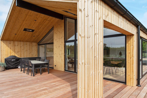 Modernes Ferienhaus in Sæby, Dänemark, mit Holzterrasse, Essbereich im Freien und großen Fenstern.