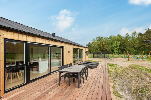 Außenterrasse eines 10-Personen-Ferienhauses in Sæby, Dänemark, mit Esstisch, Liegen und Naturausblick.