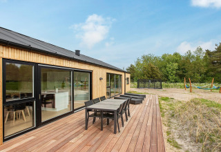 Außenterrasse eines 10-Personen-Ferienhauses in Sæby, Dänemark, mit Esstisch, Liegen und Naturausblick.