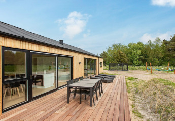 Außenterrasse eines 10-Personen-Ferienhauses in Sæby, Dänemark, mit Esstisch, Liegen und Naturausblick.