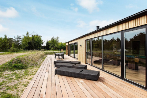 Udendørs terrasse ved 10-personers feriehus i Sæby, Danmark, med liggestole og spisebord, omgivet af natur.