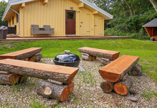 Udendørs siddeområde ved Cozy Coastal Cottage Retreat i Danmark med rustikke træbænke og grill.