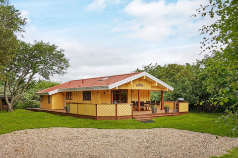 Hyggelig kystnær hytte med træterrasse, rødtag og omgivet af grøn have ved Cozy Coastal Cottage Retreat.