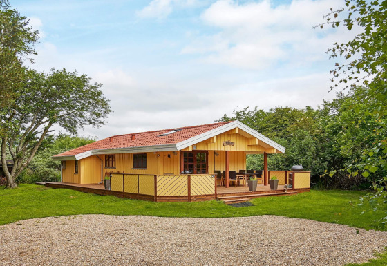 Accogliente cottage costiero giallo con tetto rosso e terrazza in legno al Cozy Coastal Cottage Retreat.