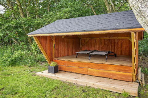Houten open hut met twee ligstoelen bij Cozy Coastal Cottage Retreat in Denemarken, naast een bos.