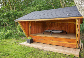 Überdachter Holzunterstand im Cozy Coastal Cottage Retreat in Dänemark mit zwei Liegen und Waldblick.