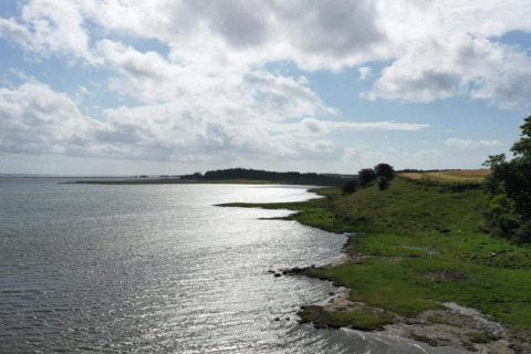 Udsigt over kystlinjen fra Cozy Coastal Cottage Retreat i Danmark med hav, grønne marker og skyer