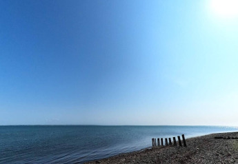 Blick auf die ruhige Küste bei Cozy Coastal Cottage Retreat in Dänemark mit blauem Wasser und klarem Himmel.