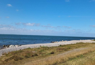 Kystbillede taget fra Cozy Coastal Cottage Retreat i Danmark med stenstrand, hav og blå himmel.
