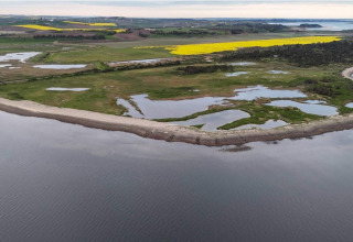 Kustlandschap met grasvelden, vijvers en zee bij Cozy Coastal Cottage Retreat, Denemarken.