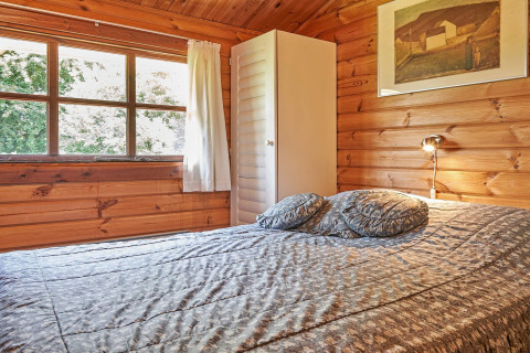 Camera accogliente con pareti in legno, grande finestra, letto e armadio al Cozy Coastal Cottage Retreat in Danimarca.