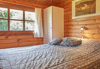 Gezellige slaapkamer met houten muren, groot raam, bed en kast bij Cozy Coastal Cottage Retreat in Denemarken.