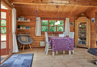 Træhytte i Danmark med spisebord, stole, vitrineskab og naturligt lys fra vinduer og terrassedør.
