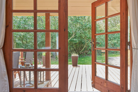 Udsigt gennem åbne glasdøre til en træterrasse og grøn have ved Cozy Coastal Cottage Retreat, Danmark.