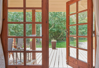 Vista attraverso porte di vetro aperte su terrazza in legno e giardino al Cozy Coastal Cottage Retreat, Danimarca.