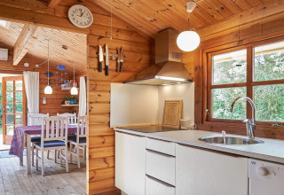 Cucina e sala da pranzo accoglienti con pareti in legno al Cozy Coastal Cottage Retreat in Danimarca, luce naturale.