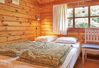 Hyggeligt soveværelse i Cozy Coastal Cottage Retreat i Danmark med trævægge, vindue og senge.
