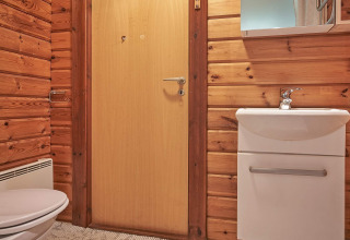 Badeværelse med trævægge, hvidt toilet og vask på Cozy Coastal Cottage Retreat i Danmark.