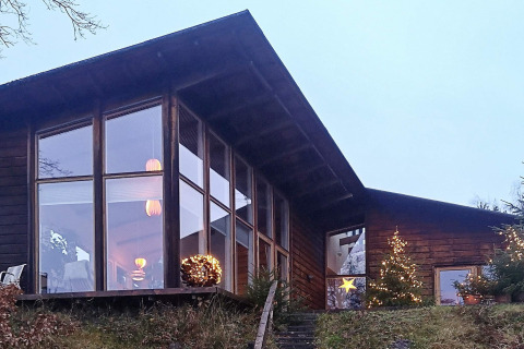Modern holiday lodge in Bryrup, Denmark, featuring large windows and Christmas lights at dusk.