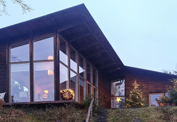 Cabaña moderna de vacaciones en Bryrup, Dinamarca, con grandes ventanales y luces navideñas de noche.