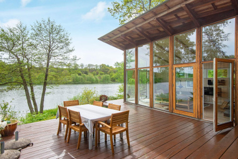 Lake view from the terrace of the 6 person holiday home in Bryrup, Denmark, with large windows and dining set.