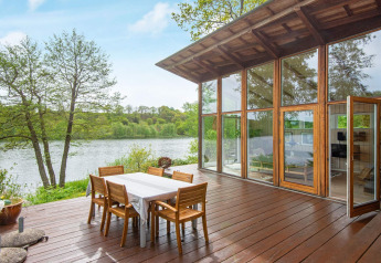 Vista al lago desde la terraza de la casa de vacaciones para 6 personas en Bryrup, Dinamarca, con ventanales y mesa.