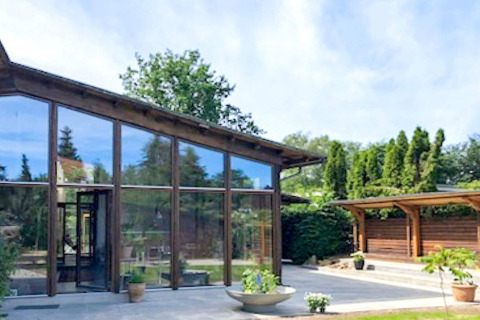 Moderne feriebolig i Bryrup, Danmark med store glasvinduer, terrasse og grøn have i baggrunden.