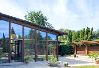 Modern holiday home in Bryrup, Denmark with large glass windows, patio, and lush garden background.