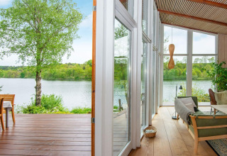 Blick aus einem Ferienhaus am See bei Bryrup, Dänemark, mit Terrasse und modernen Glaswänden.