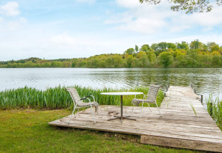 Wooden deck with table and chairs by the lake at 6 person holiday home in Bryrup, Denmark, scenic view.